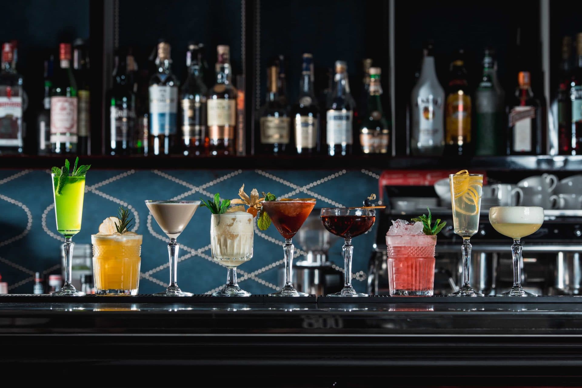 A range of different cocktails sit on a home bar in a variety of glasses.