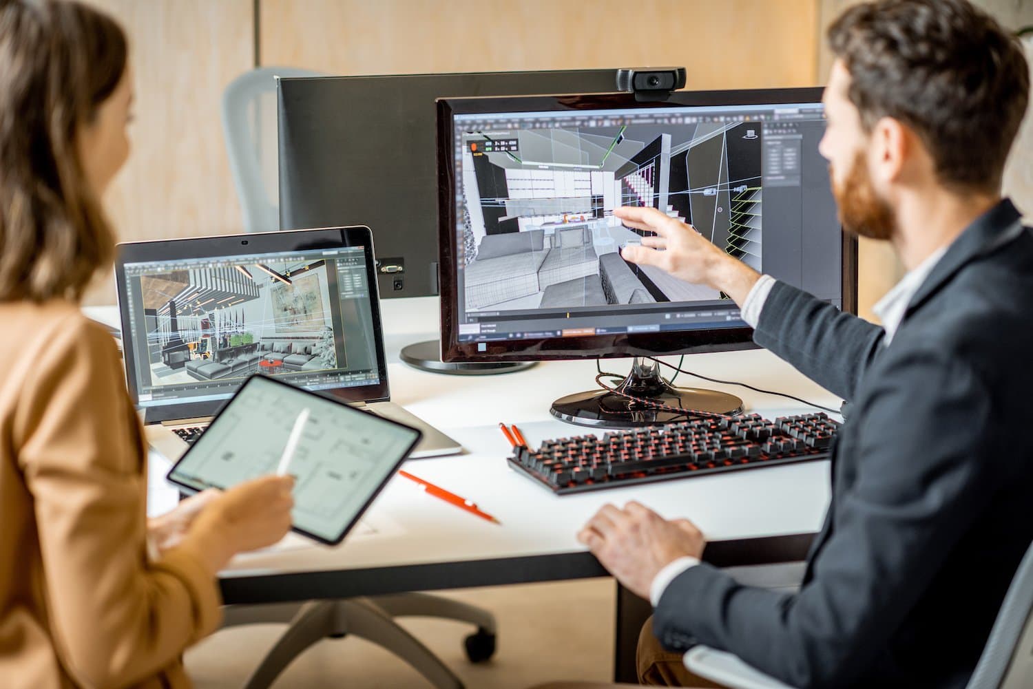 Two interior designers work at a desk where they have 3D renderings of home interiors on their screens.