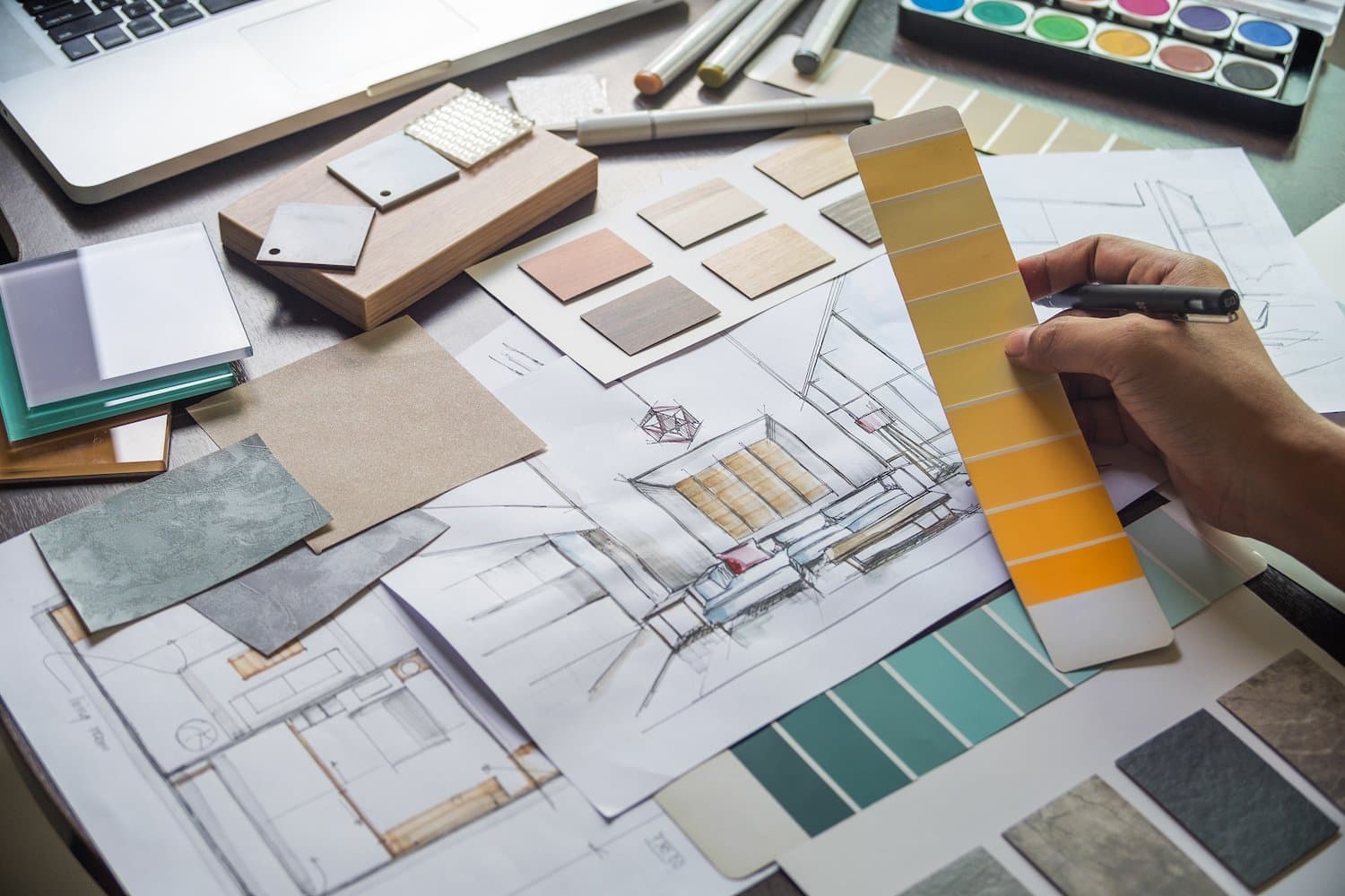 Interior designer sits at their desk with a spread of paint, tile, and fabric swatches in front of them. There's also a