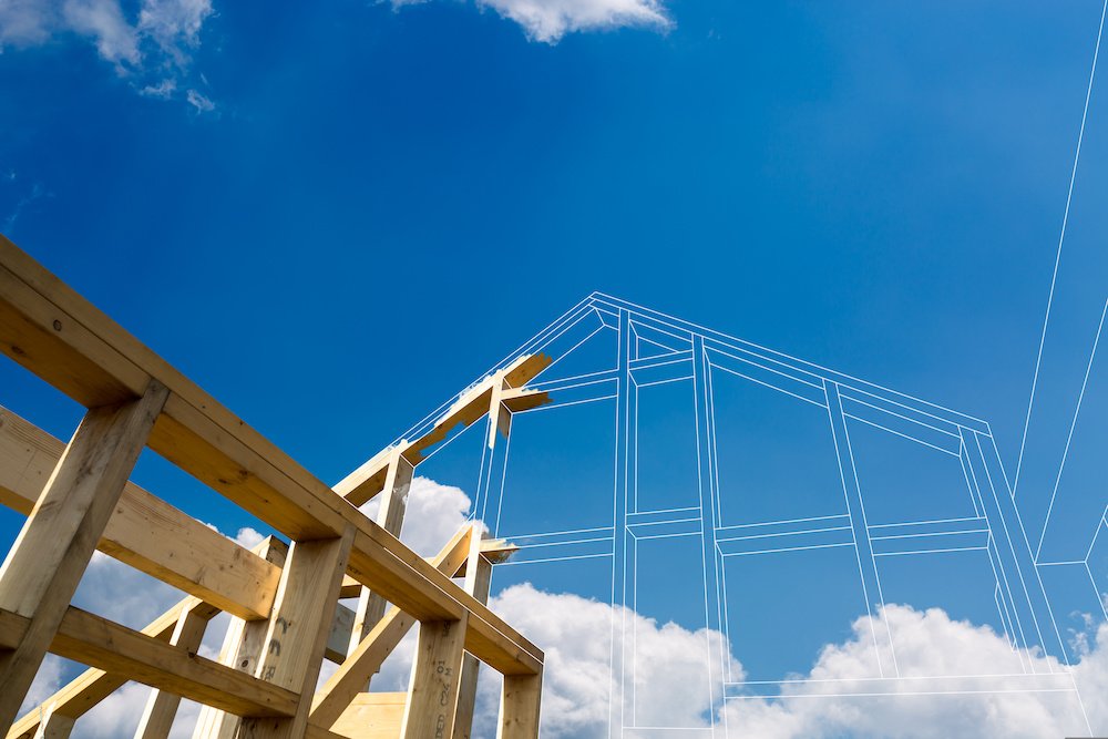 A view of the wooden beams of a home being built, with digital lines continuing the rest of the construction to show what it will look like. The sky above is blue.